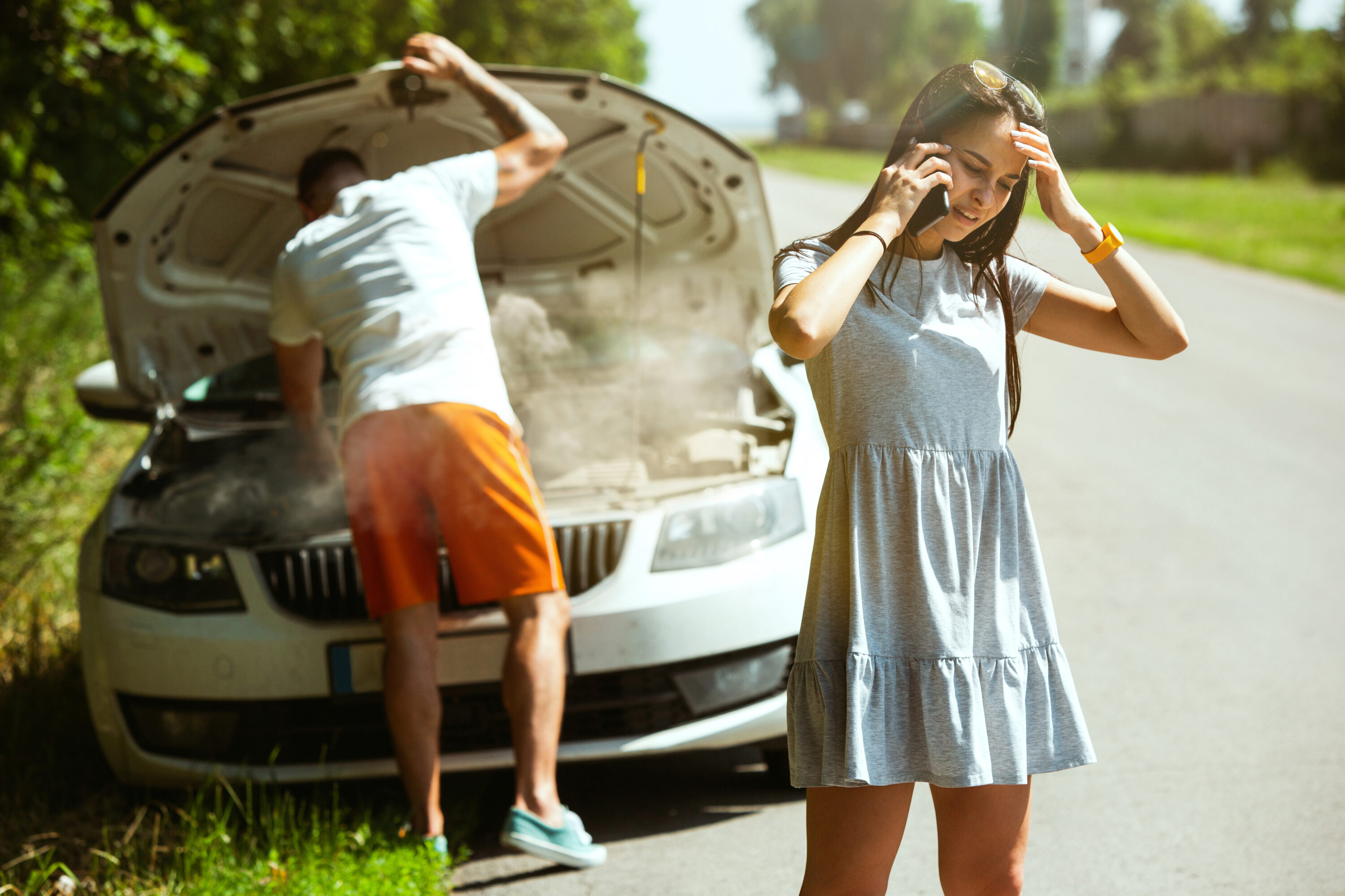 Un jeune couple voyageant en voiture par une journée ensoleillée, arrêtés sur le bord route pour réparer une voiture, avec une vue lumineuse et des éléments naturels à l'arrière-plan.