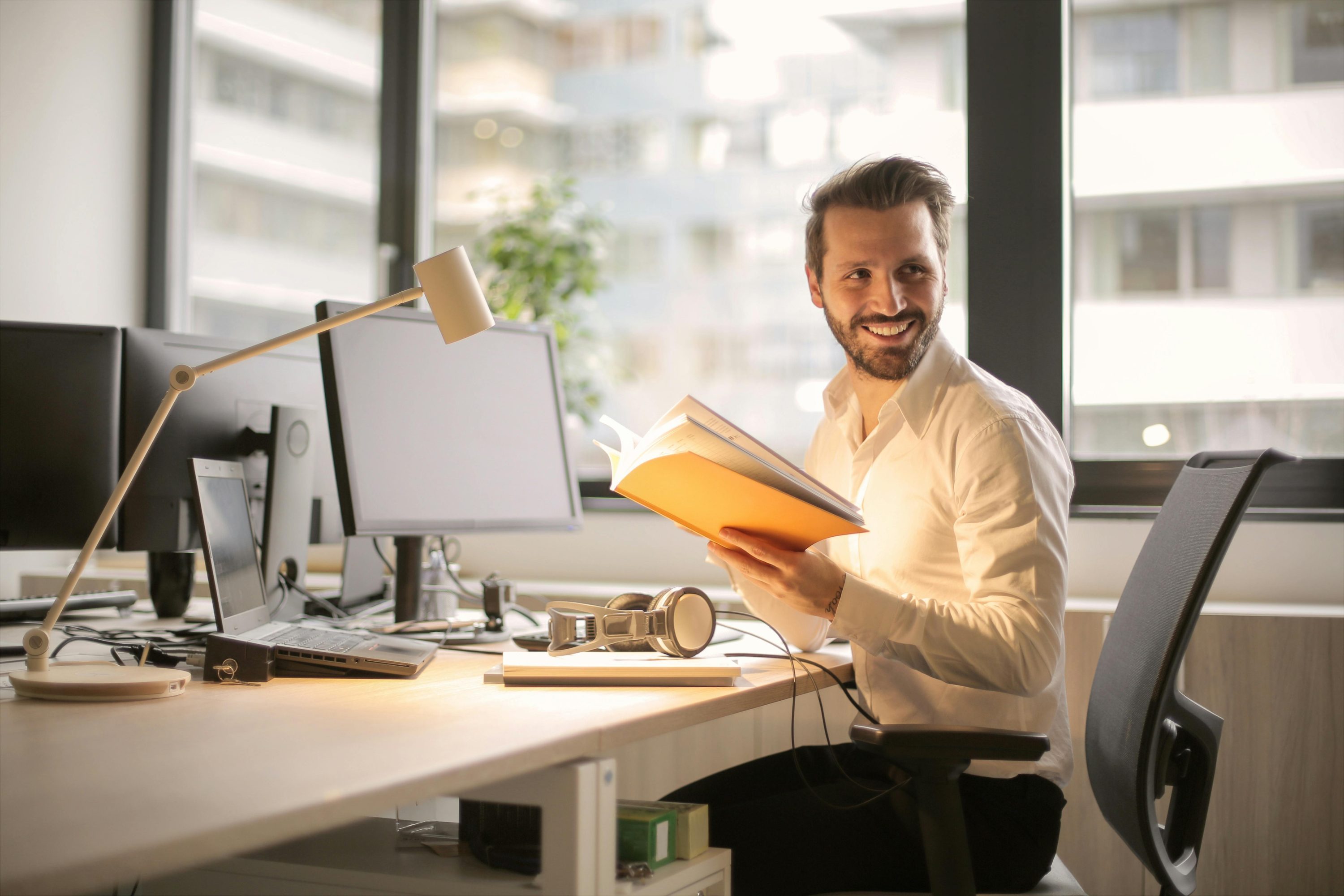 Homme souriant tenant un livre ouvert, posant dans un environnement lumineux et détendu, illustrant la lecture et l'apprentissage.